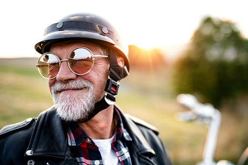 A front, view portrait of cheerful senior man traveller with motorbike in countryside, headshot.