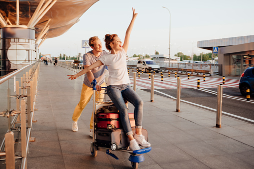 Joyful man is pushing trolley with baggage and his girlfriend on their way to airport. Website banner