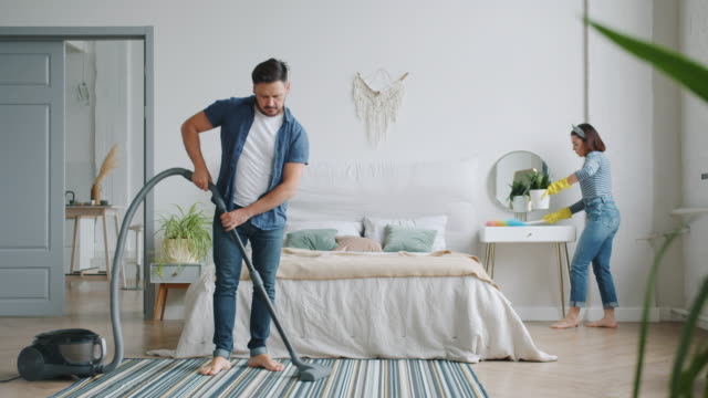 Man and woman busy with housework in bedroom cleaning room with vacuum cleaner
