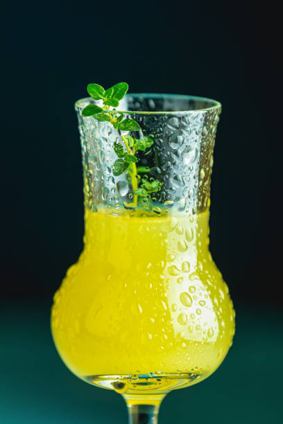 istock Limoncello with thyme in grappas wineglass with water drops close up on dark background, shallow depth of the field. 1183950690