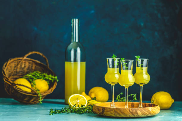 istock Limoncello with thyme in three grappas wineglass in wooden tray, fresh lemon in basket on dark blue background 1183950708