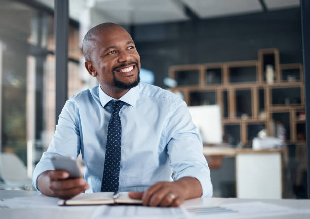 My plans are coming together so well today Shot of a mature businessman looking thoughtful while using a cellphone in an office business man looking away stock pictures, royalty-free photos & images