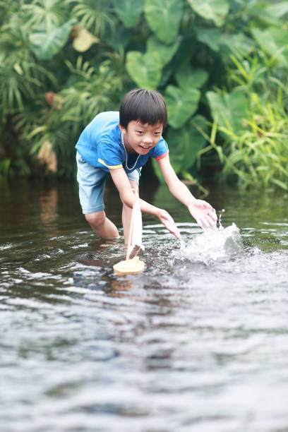 istock Boy plays with toy sailboat in water 1183954765