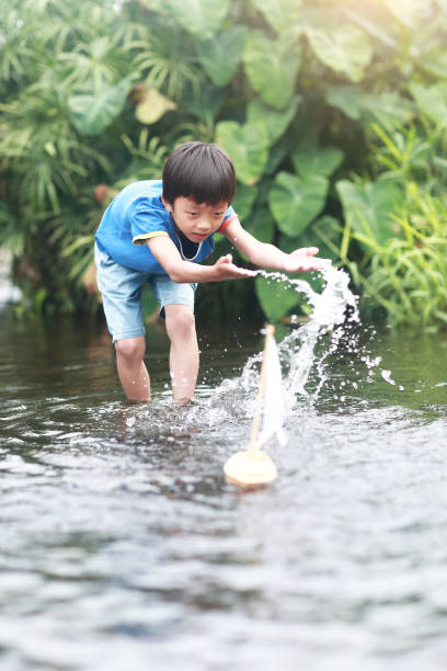 istock Boy plays with toy sailboat in water 1183954865