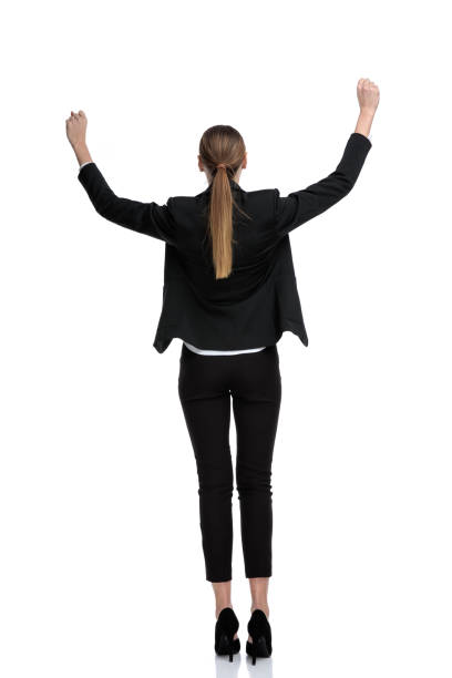 businesswoman standing with raised hands and victorious in rear view rear view of a businesswoman wearing black suit standing with raised hands and victorious against white studio background arms raised women business full length stock pictures, royalty-free photos & images