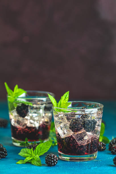 istock Refreshing summer drink with syrup, blackberry and ice on dark blue concrete background 1183957178