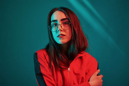 In glasses. Studio shot indoors with neon light. Portrait of beautiful young girl.