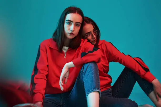 Photo of Sits on the floor. Studio shot indoors with neon light. Photo of two beautiful twins