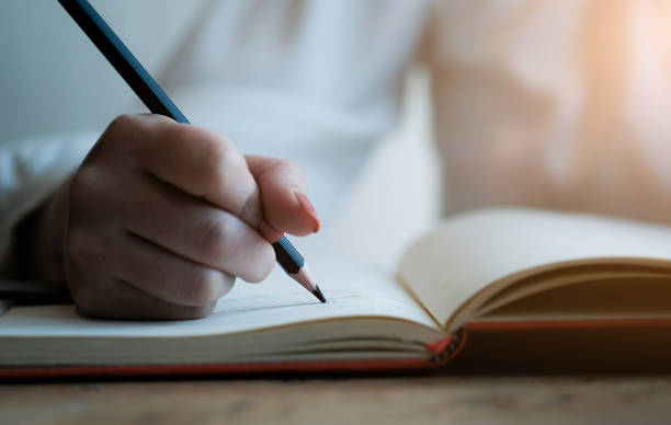 istock Woman hand with pencil writing on notebook. making notes in notebook with pencil. People writing on notebook and work on wooden table 1183959115