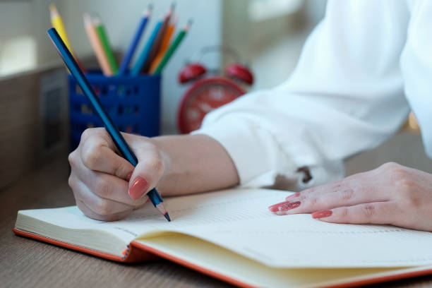 istock Woman hand with pencil writing on notebook. making notes in notebook with pencil. People writing on notebook and work on wooden table 1183959125