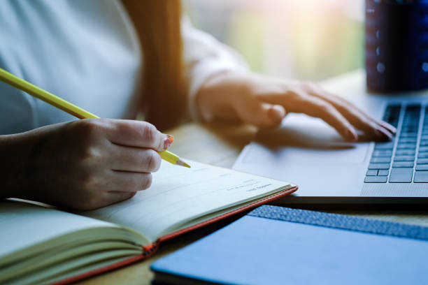 istock Woman hand with pencil writing on notebook. making notes in notebook with pencil. People writing on notebook and work on wooden table 1183959166
