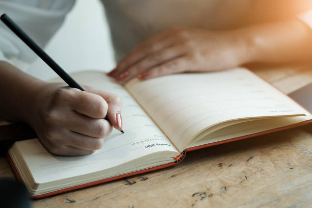 istock Woman hand with pencil writing on notebook. making notes in notebook with pencil. People writing on notebook and work on wooden table 1183959180