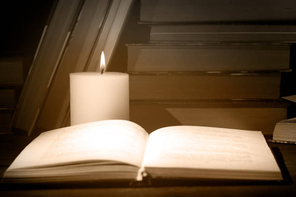 istock An open book with lighting candle flame at night on a wooden table. 1183959788