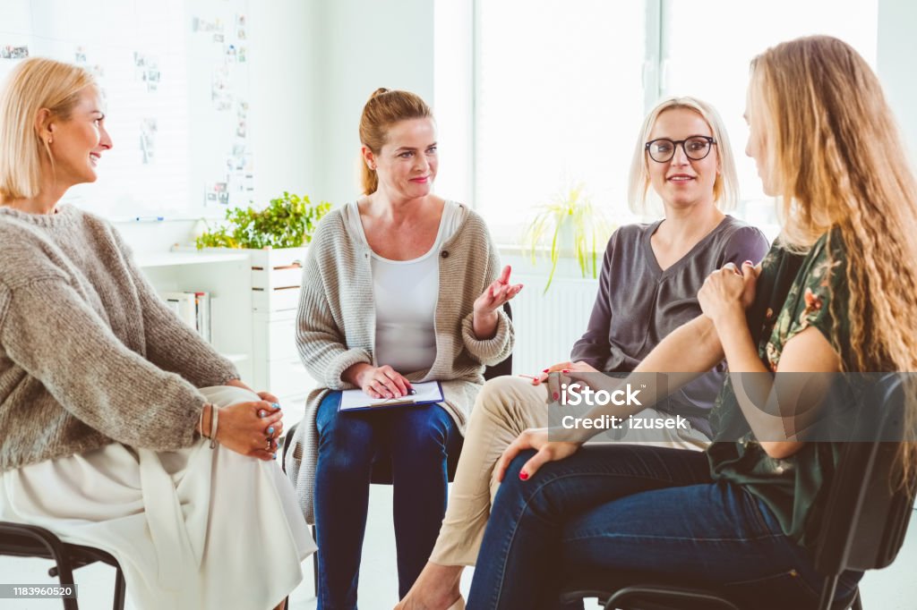 Professional discussing with group in therapy Mental health professional discussing with group. Females are sharing experiences at therapy session. They are sitting in wellness center. 35-39 Years Stock Photo