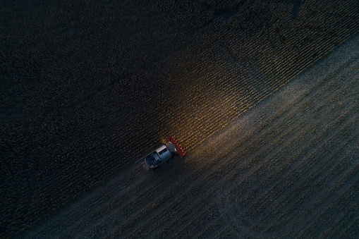 Drone Point of View. Agricultural Activity. Agricultural Combine Harvester Working in a Vast Corn Field Working at Night and Gathering the Crop. Illuminated