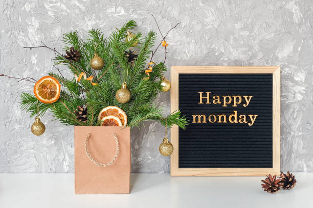 Happy Monday text on black letter board and festive bouquet of fir branches with christmas decor in craft package on table. Template for postcard, greeting card Concept Hello winter Monday stock photo