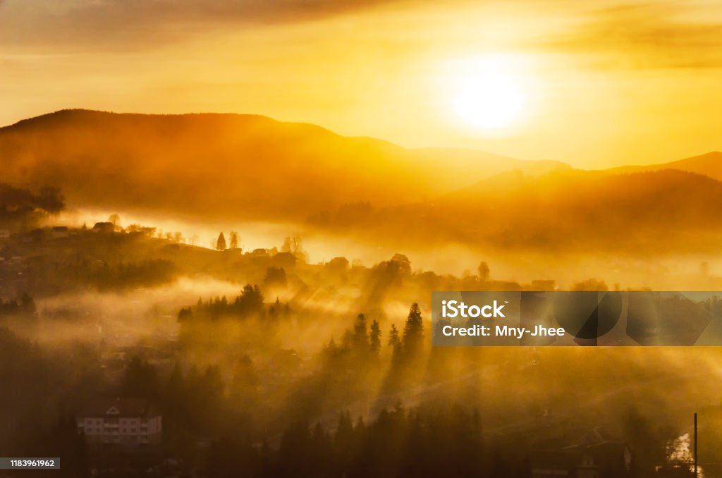 Fantastic sunrise in a mountain village with sunrays passing through a foggy hills Autumn Stock Photo