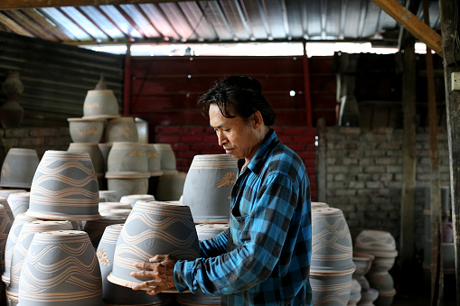 A Myanmar ethnicity male adult is showing vases in traditional pottery factory in Perak, Malaysia.