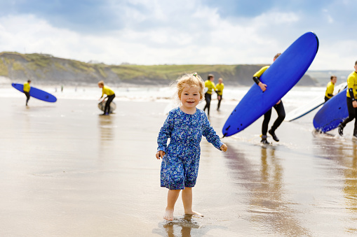 Little cute toddler girl at the Ballybunion surfer beach, getting up on surfboard for the first time, west coast of Ireland