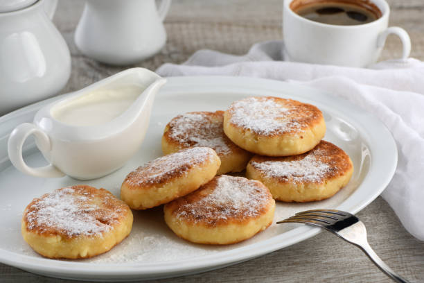 istock Breakfast. Cheese pancakes with sour cream sprinkled with powdered sugar on a white plate. 1183965336