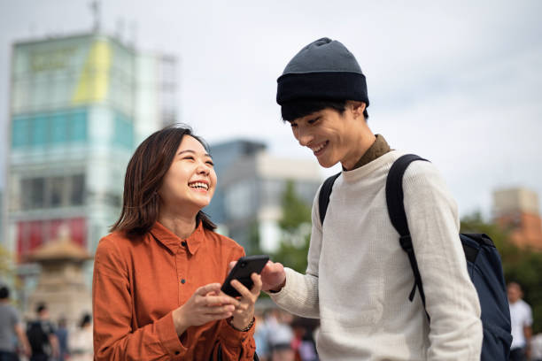 młoda para patrząc na inteligentny telefon na ulicy - harajuku district zdjęcia i obrazy z banku zdjęć