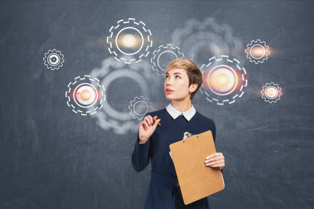 istock Woman with clipboard, gears on blackboard 1183967576