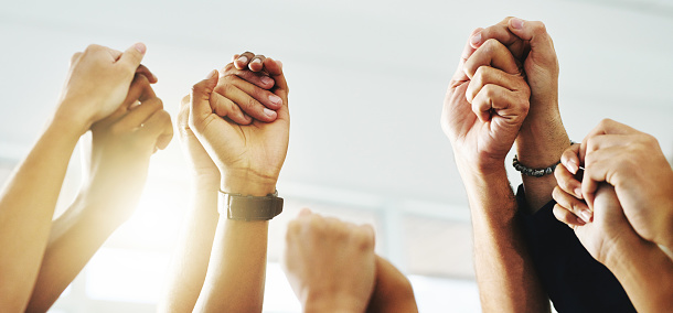 Closeup shot of a group of unrecognizable businesspeople holding hands while raising their arms
