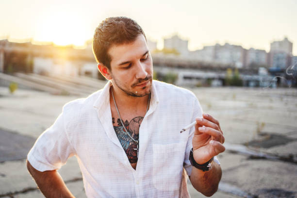 istock Man wearing white shirt and smoking cigarette at sunset. 1183971386