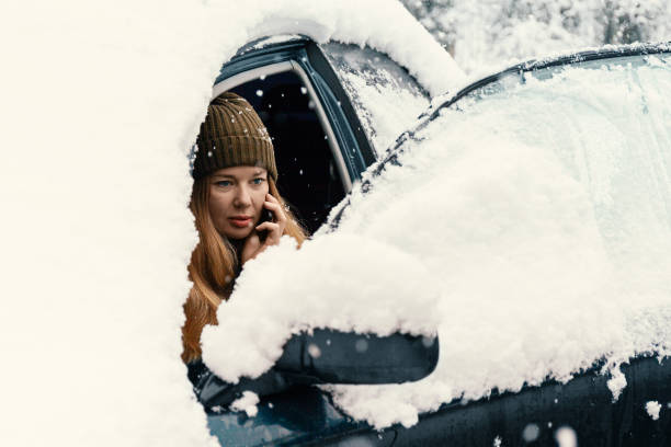 istock Young woman calling for help or assistance inside snow covered car.  Engine start in frost. Breakdown services in the winter 1183971707