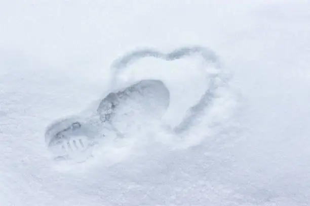 Photo of Heart drawing in the snow. Footprint and silhouette of the heart. Winter concept broken heart, unhappy love, coldness dislike