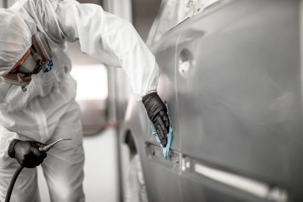 Car repair technician blowing off excess particles from a painted segment on a car's quarter panel in a car painting chamber Car painter dusting off a freshly painted car segment in a painting booth of a repair shop. door panel stock pictures, royalty-free photos & images