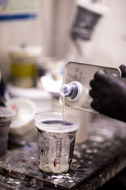 pouring a paint thinner in a mixing container in a workshop - automobile industry transportation indoors vertical imagens e fotografias de stock