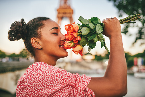 Shot of an attractive young woman smelling a bouquet of lovely roses outdoors in Paris, France
