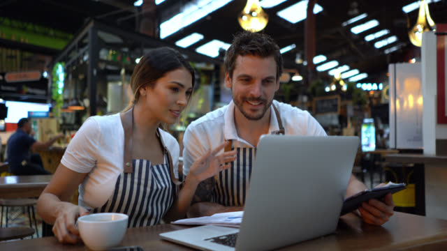 Happy business owners of a restaurant doing the books using a laptop and paperwork-