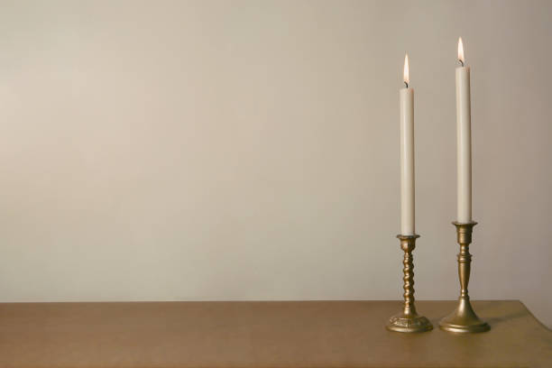 istock Two candles burning in vintage candlesticks on table against empty wall. 1183988290