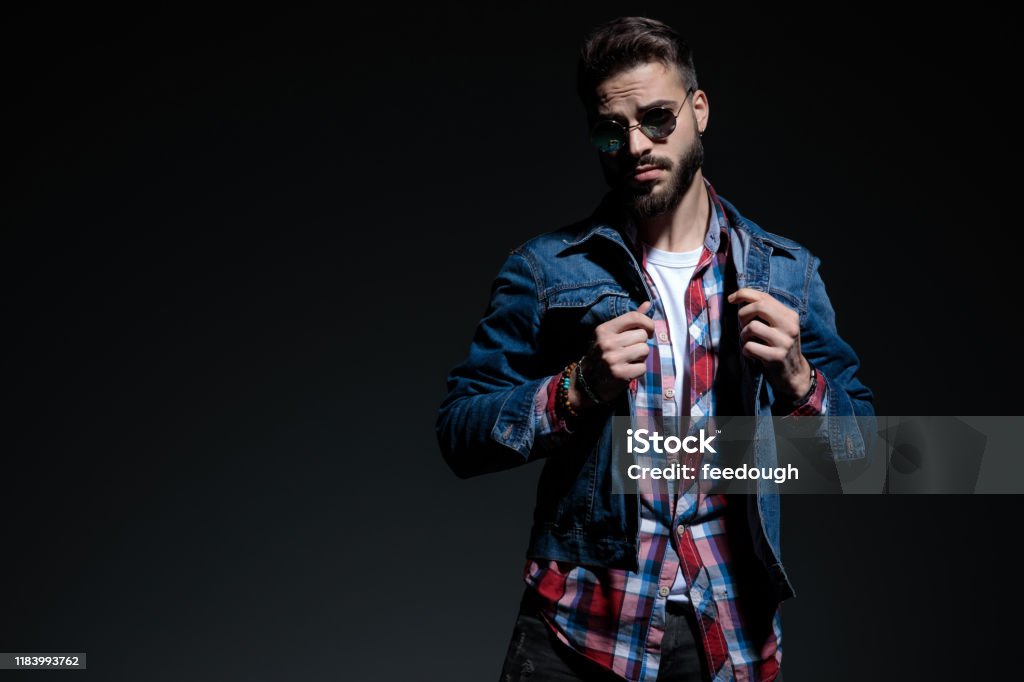 Determined casual man holding both fists clenched Determined casual man holding both fists clenched  and looking forward while wearing sunglasses, jeans jacket and a checkered shirt, standing on black studio background 20-29 Years Stock Photo