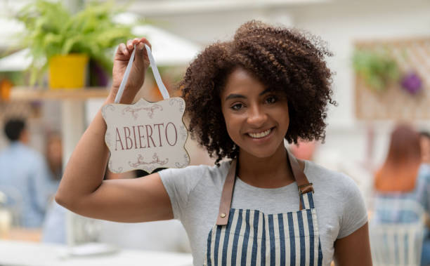 istock Waitress at a restaurant holding an open sign in Spanish 1183994180