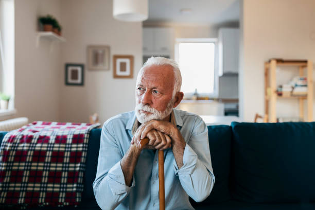 Elderly man sitting alone at home Hands of a thoughtful old man leaning on a cane, sitting at home. old man depressed stock pictures, royalty-free photos & images