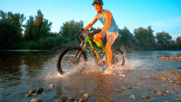 istock CLOSE UP: Cheerful mountain biker riding in the stream and splashing water. 1183999745