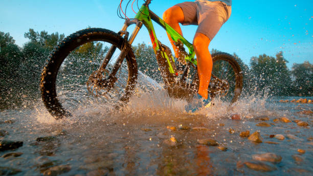 istock LOW ANGLE: Unrecognizable mountain biker rides past camera in the river shallows 1183999825