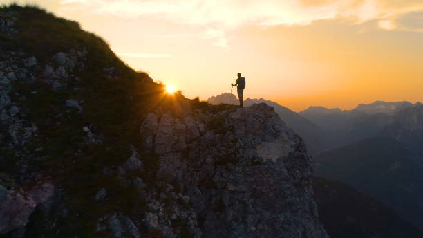 istock LENS FLARE: Stunning sunset illuminates the Alps and hiker standing on a cliff. 1183999958