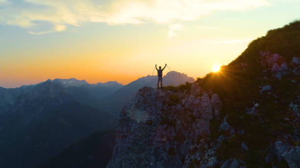 istock DRONE: Golden morning sun rays shine on excited trekker standing on a cliff. 1183999959