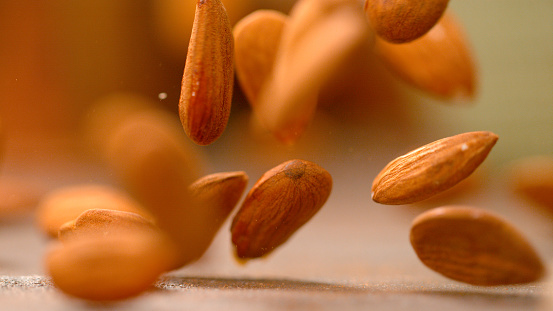MACRO, DOF: Healthy almond kernels fall from the sky and bounce off the kitchen table. Homegrown organic almonds bouncing around the empty kitchen counter. Ripe unpeeled brown almonds falling down.