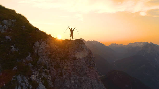 istock AERIAL: Flying behind man celebrating a successful ascent onto a scenic cliff. 1184000388