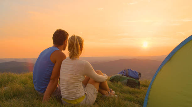 istock SUN FLARE: Unrecognizable couple sitting in the grass and watching the sunset. 1184000413