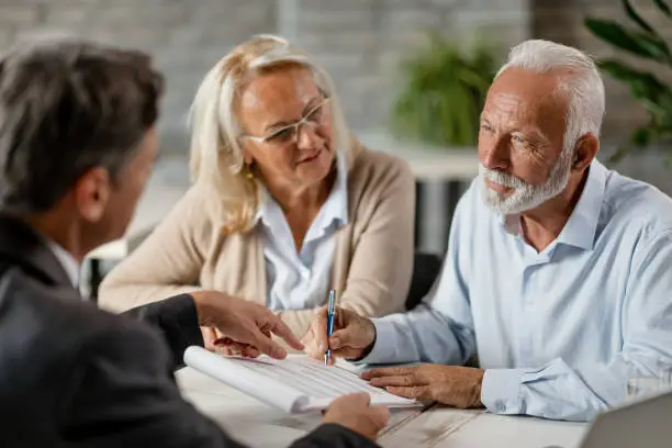 Mature couple having a meeting with bank manager and signing lease agreement in the office. Focus is mature man.