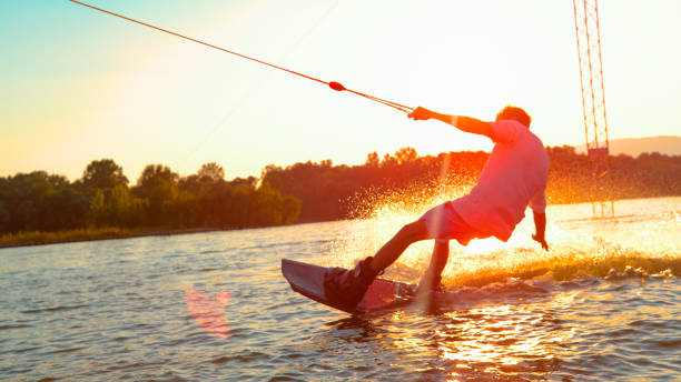 sun flare: unkenntlich athletischer mann weckt auf dem see bei goldenem sonnenuntergang. - wakeboarding stock-fotos und bilder