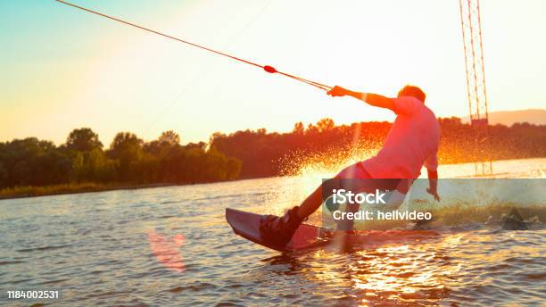 Sun Flare Unrecognizable Athletic Man Wakesurfing On The Lake At Golden Sunset Stock Photo - Download Image Now