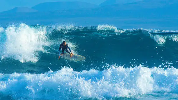 Big barrel wave pushes the young Caucasian surfer towards the coastline of the picturesque Canary Islands. Stoked surfer dude enjoying his summer in Fuerteventura by carving big splashing ocean waves.