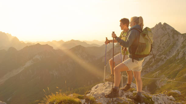 istock SUN FLARE: Young couple standing on the mountaintop and watching the sunset. 1184004299